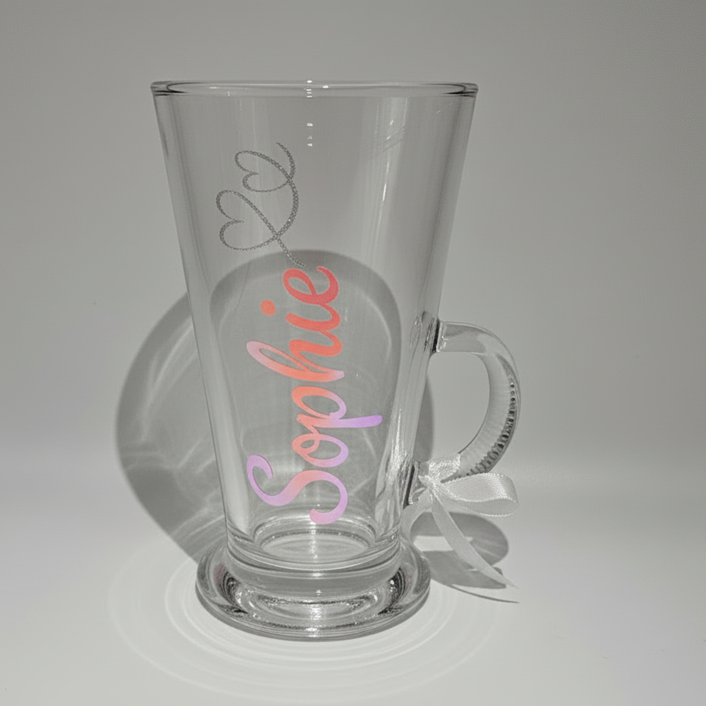 Personalised clear glass mug with the name 'Sophie' on it in a pink & coral holographic vinyl against a plain background.