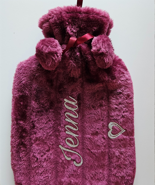 Plum fluffy faux fur hot water bottle with the name 'Jenna' in a silver glitter vinyl & pom poms on a white background