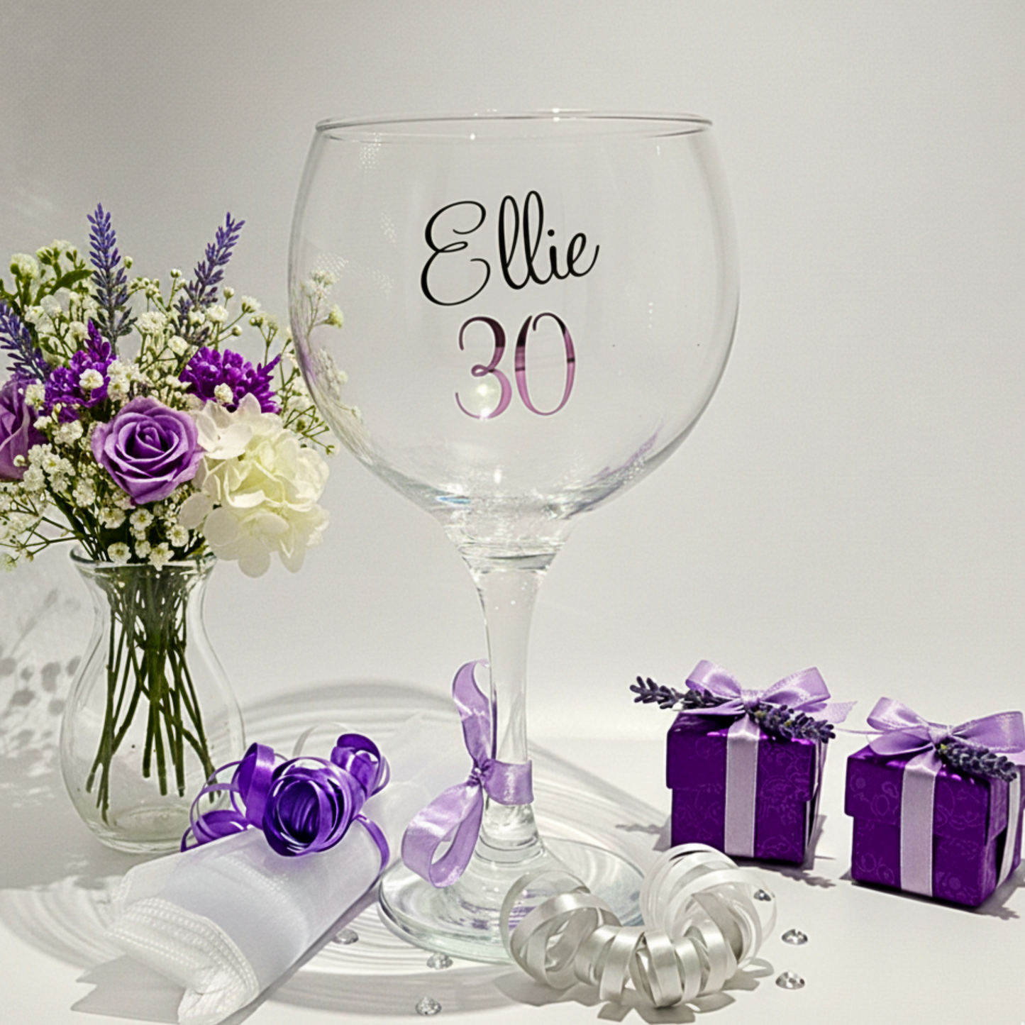 Clear balloon glass with the name 'Ellie' 30 in purple pink vinyl. On a clean background with gift box & flowers