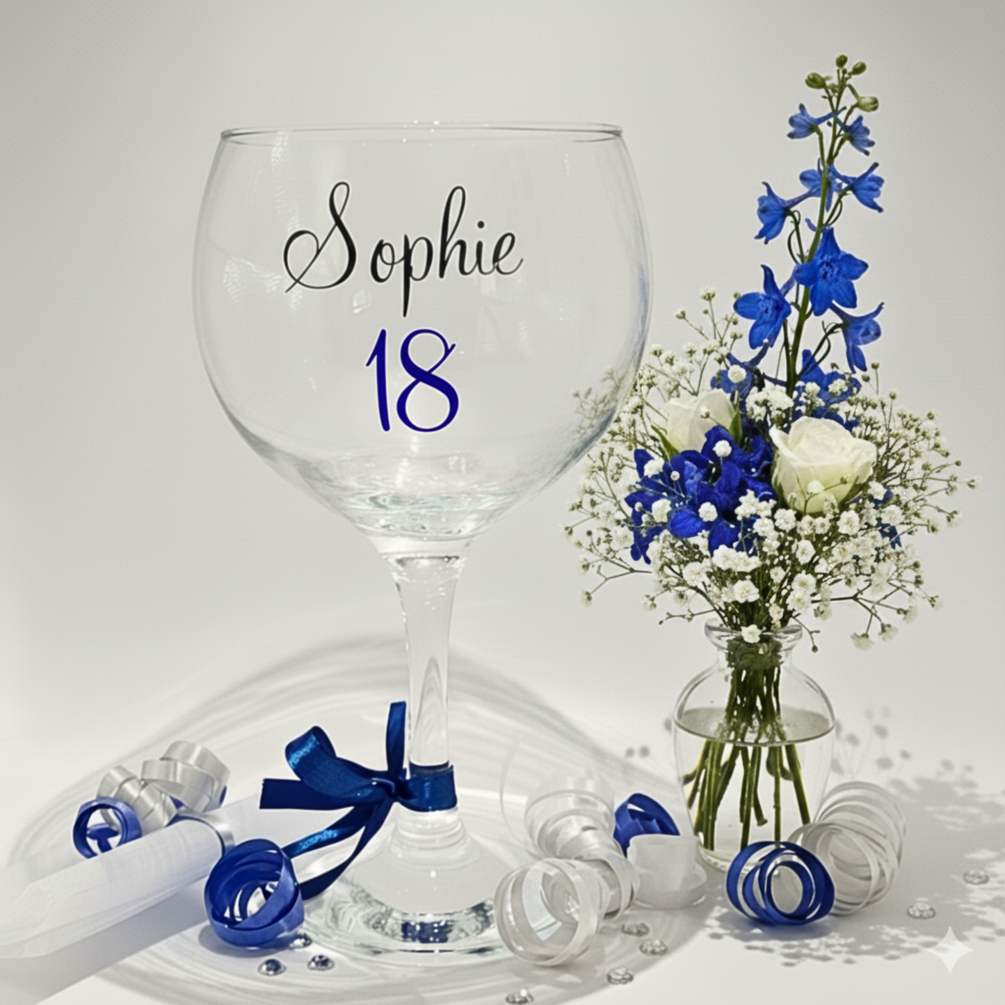 Gin glass with 'Sophie' 18 on a white background with blue flowers in a clear vase