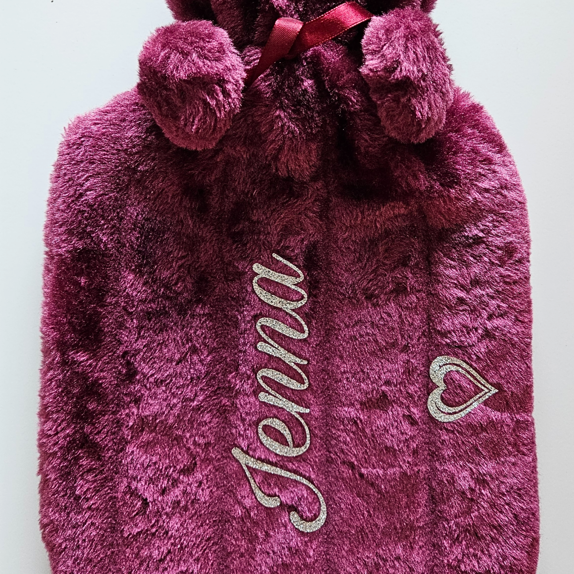 Plum plush hot water bottle bag with 'Jenna' vinyl on it, featuring pom-poms and a heart design.