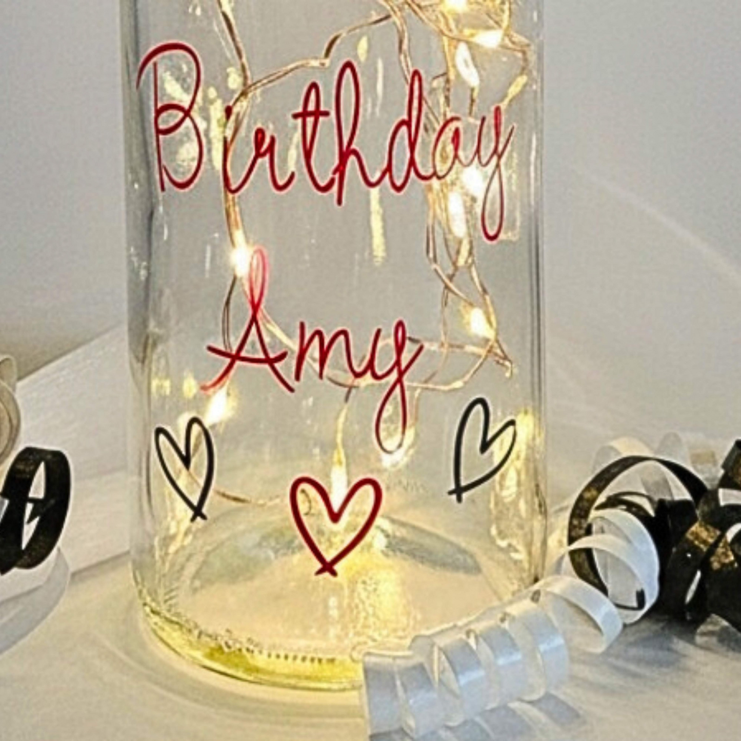 The bottom of a personalised LED light up glass bottle with 'Birthday Amy' in pink text on a white surface.
