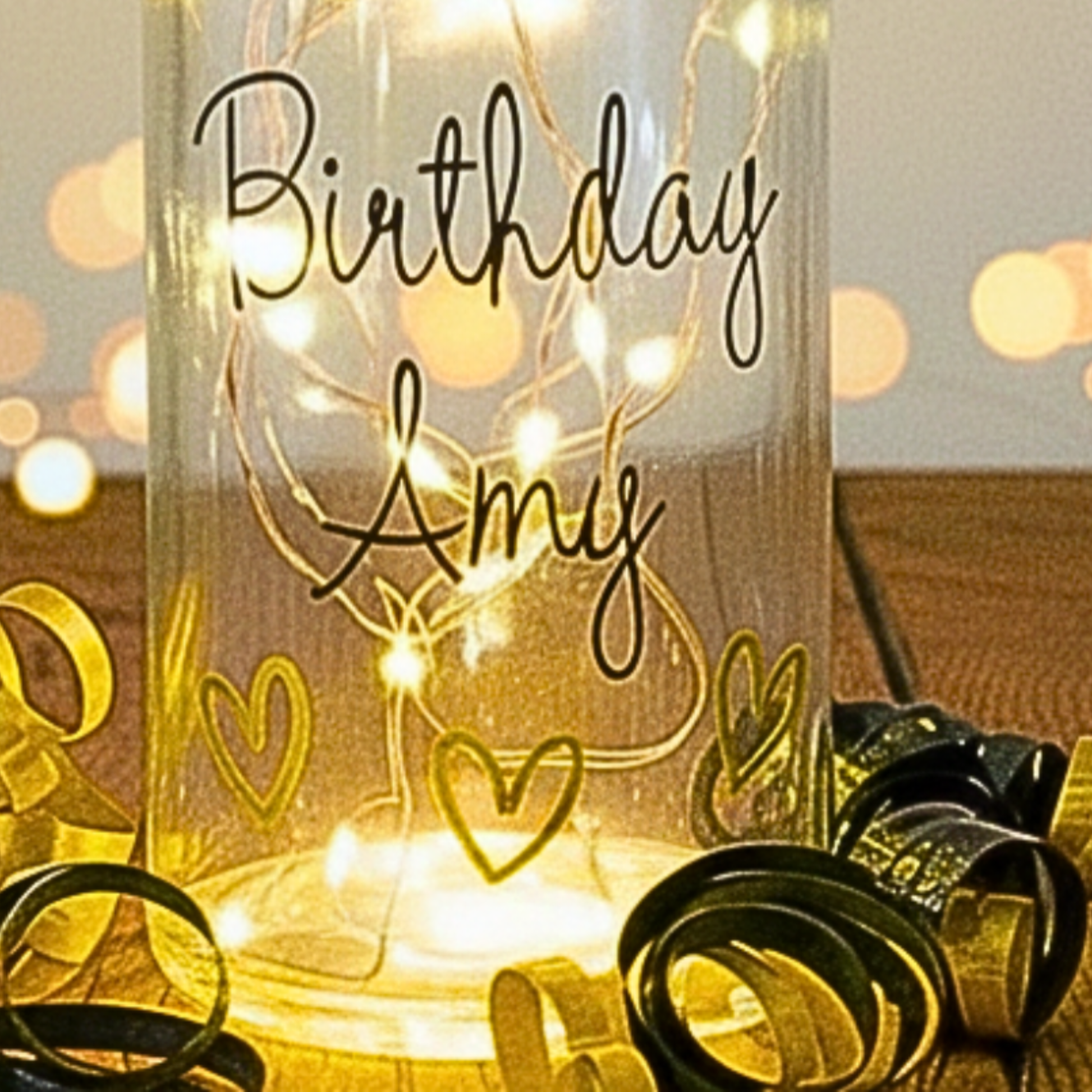 The bottom of a personalised LED light up glass bottle with the text 'Birthday Amy' & gold & black satin curling ribbons around