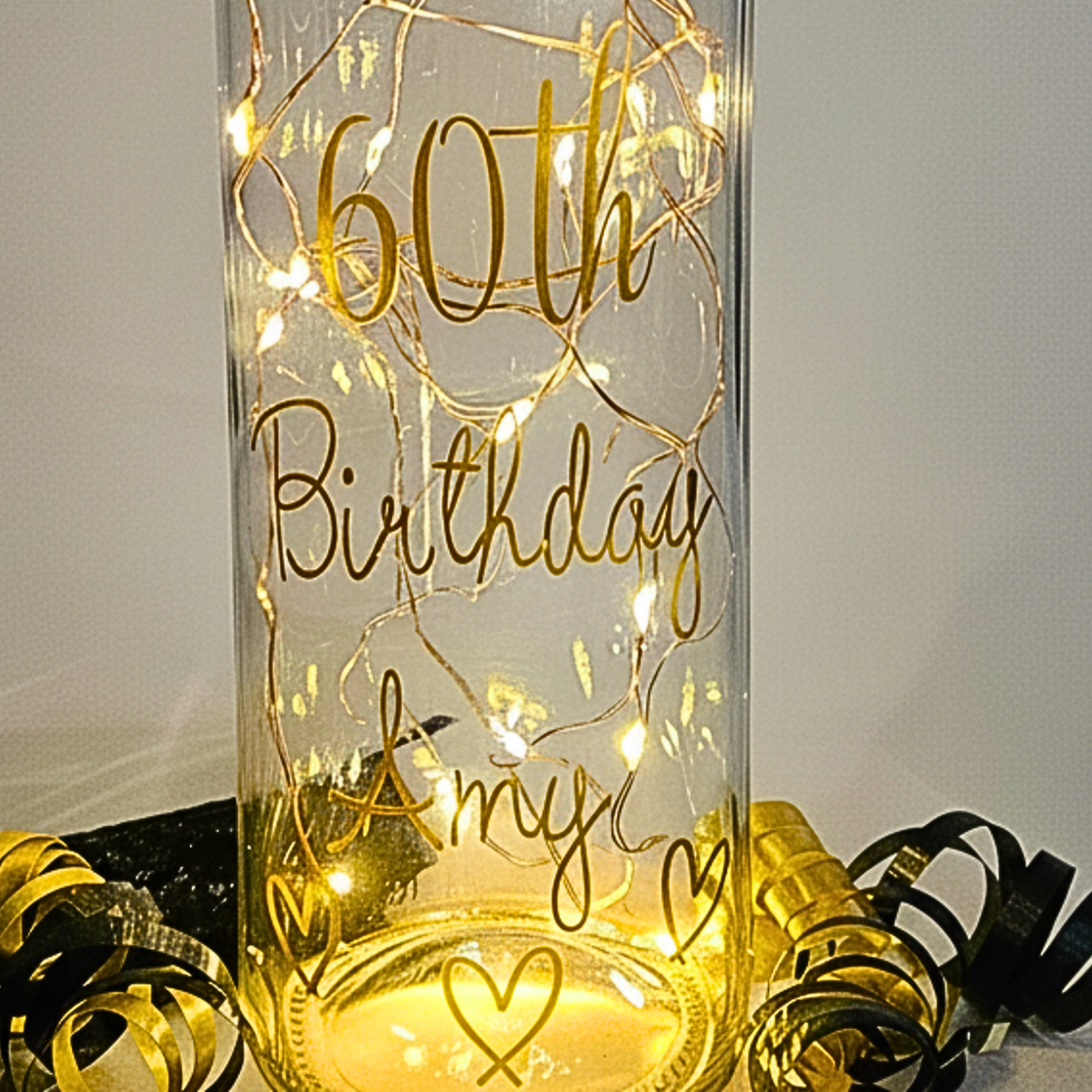 The bottom of a personalised LED light up bottle with '60th Birthday Amy' gold text on a neutral background