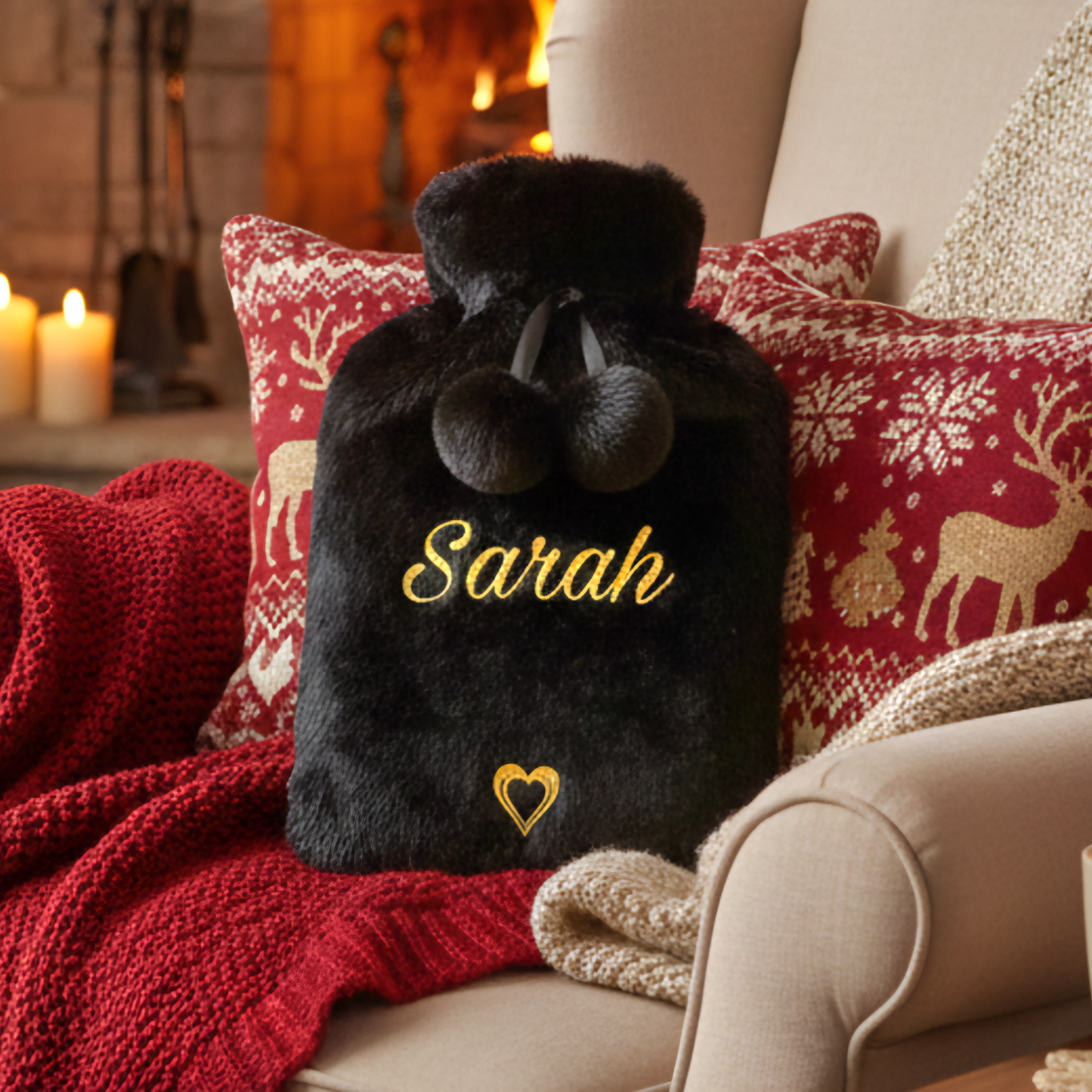 Black plush hot water bottle with 'Sarah' and a heart on a red cushion in a cozy living room.