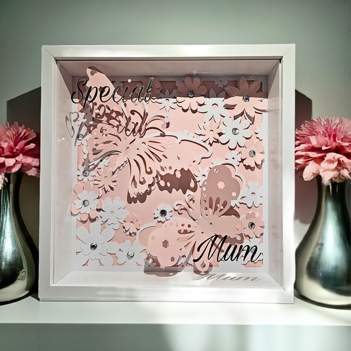 Personalised 3D shadow box with 'Special Mum' text in silver vinyl on a glass front. Has a pink & white cardstock butterfly, floral design in a white frame placed between two vases with pink flowers.