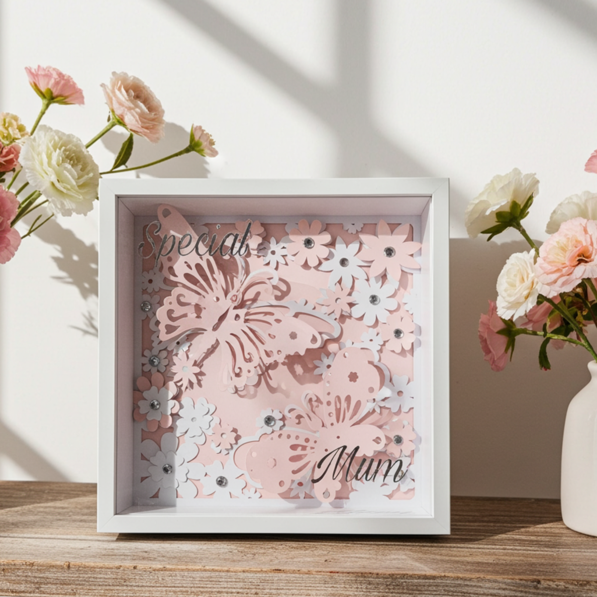 Personalised shadow box with the text 'Special Mum' on a glass front. Features a pink butterfly & floral display with a clear rhinestone finish. Showcased in a sleek white acrylic frame on a shelf inbetween vases of pink flowers.
