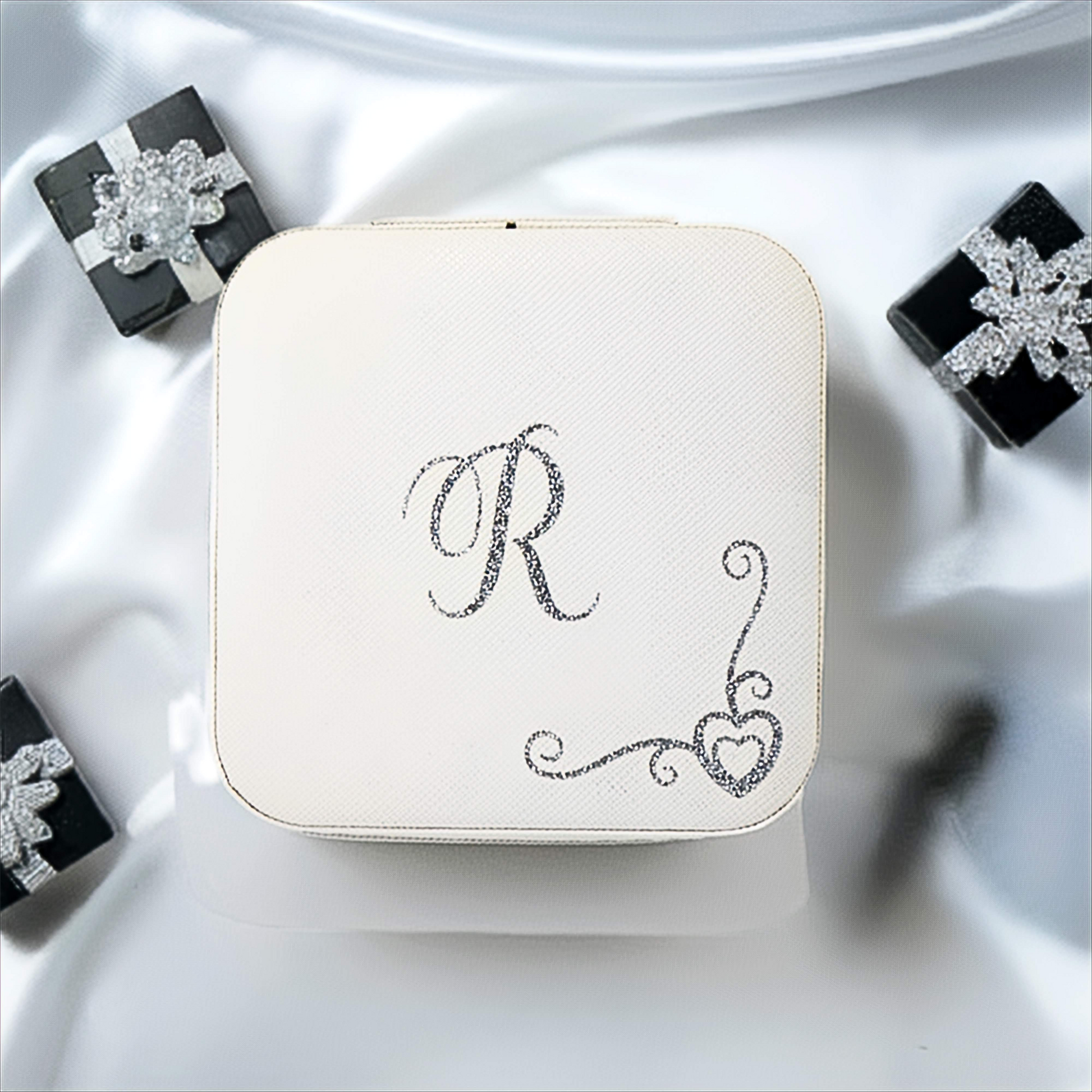 White jewelry box with 'R' monogram on a white fabric background