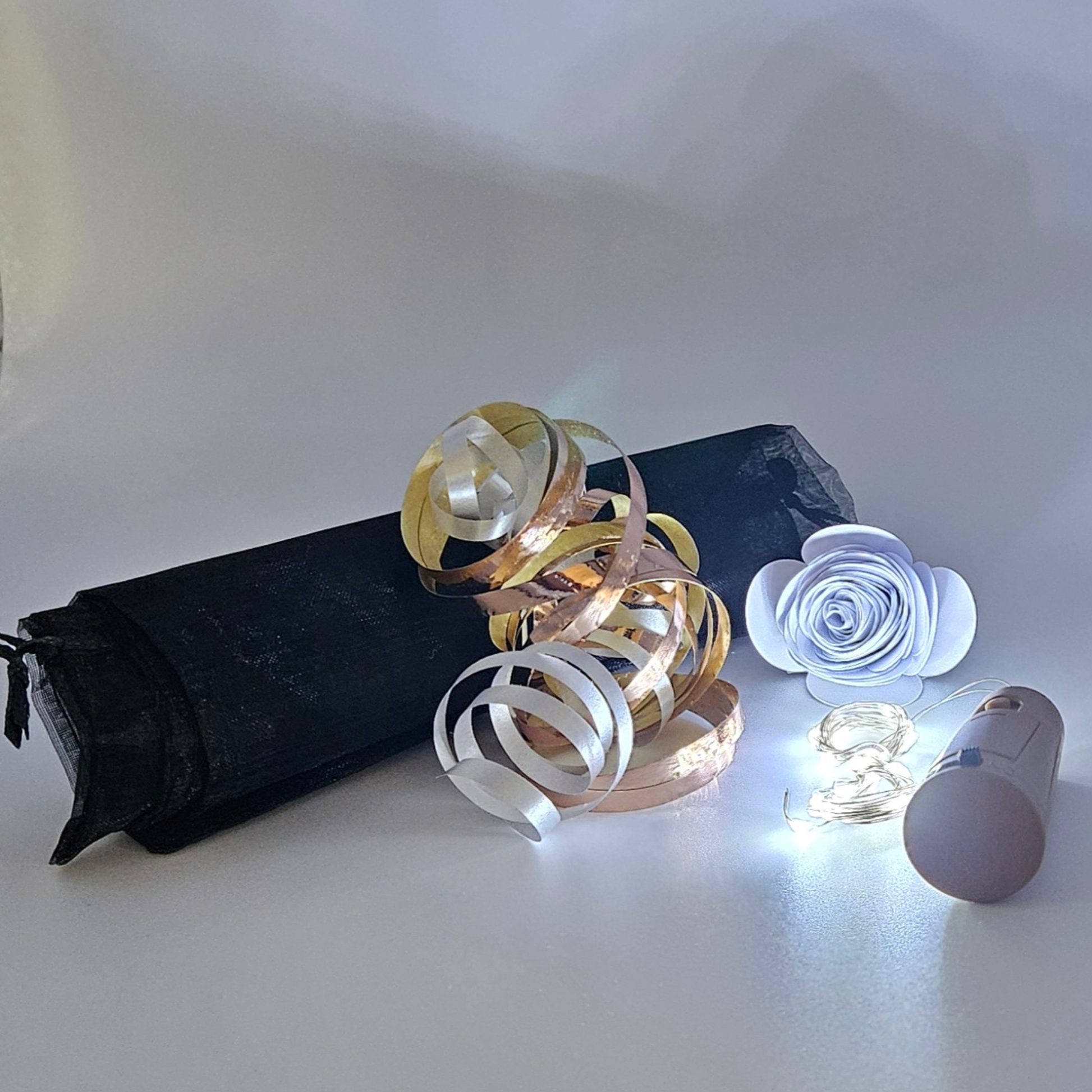 Ice white LED bottle lights next to an organza gift bag with rose gold & silver satin curling ribbons on a plain background.