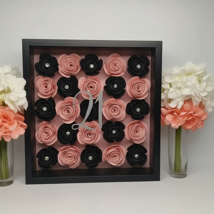 Personalised shadow box with pink and black flower roses in a black frame, surrounded by flowers.