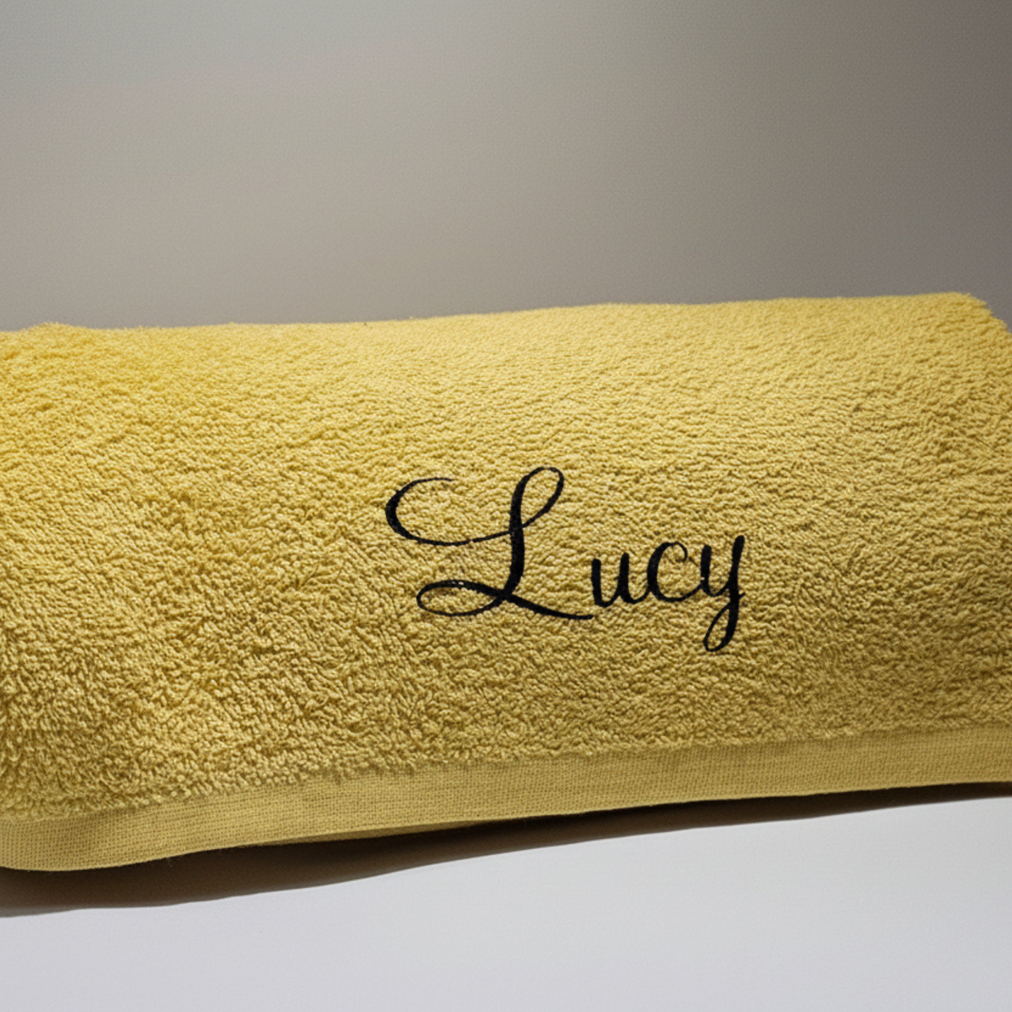 Personalised gold yellow beach towel with the name 'Lucy' on it in black glitter vinyl against a neutral background