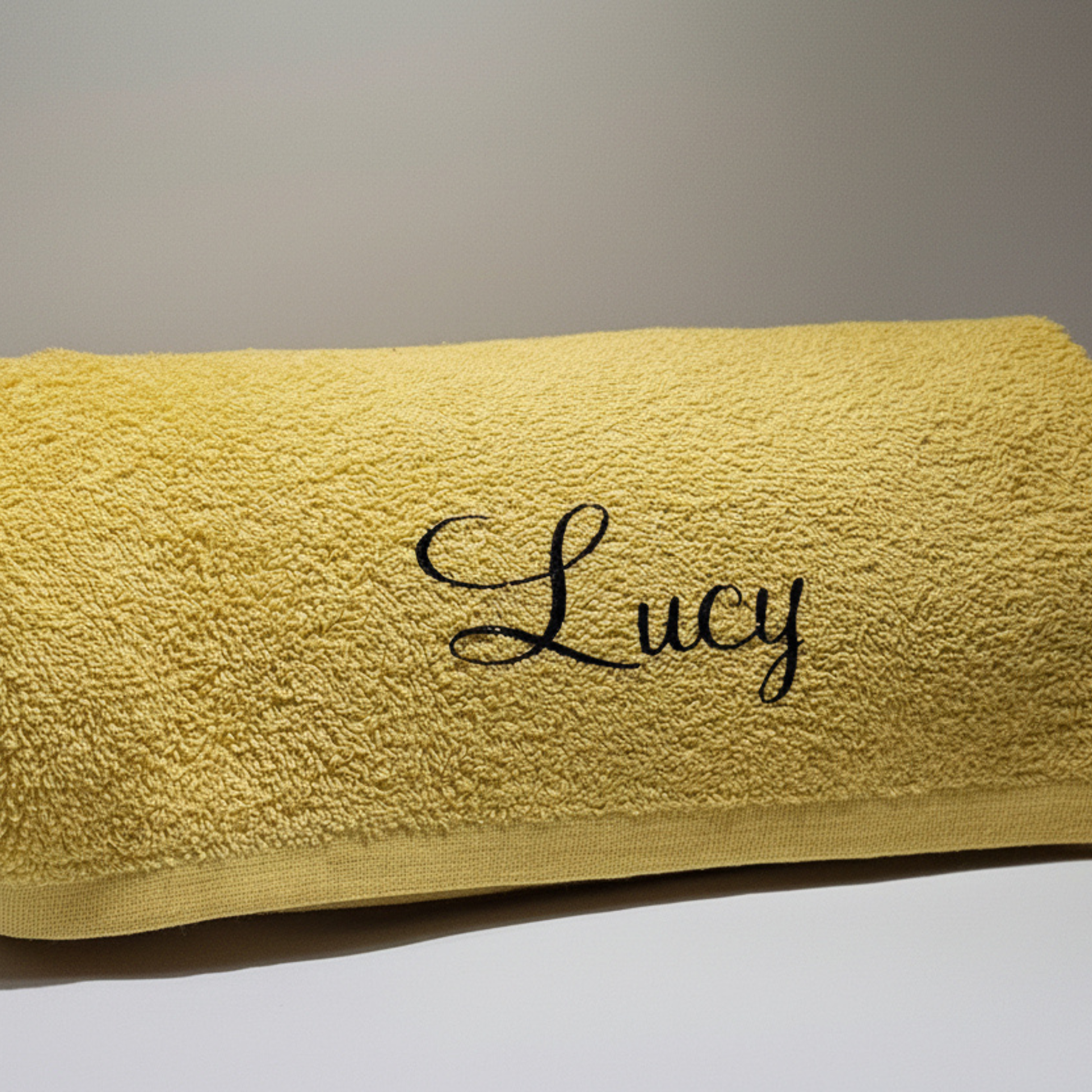 Personalised gold yellow beach towel with the name 'Lucy' on it in black glitter vinyl against a neutral background