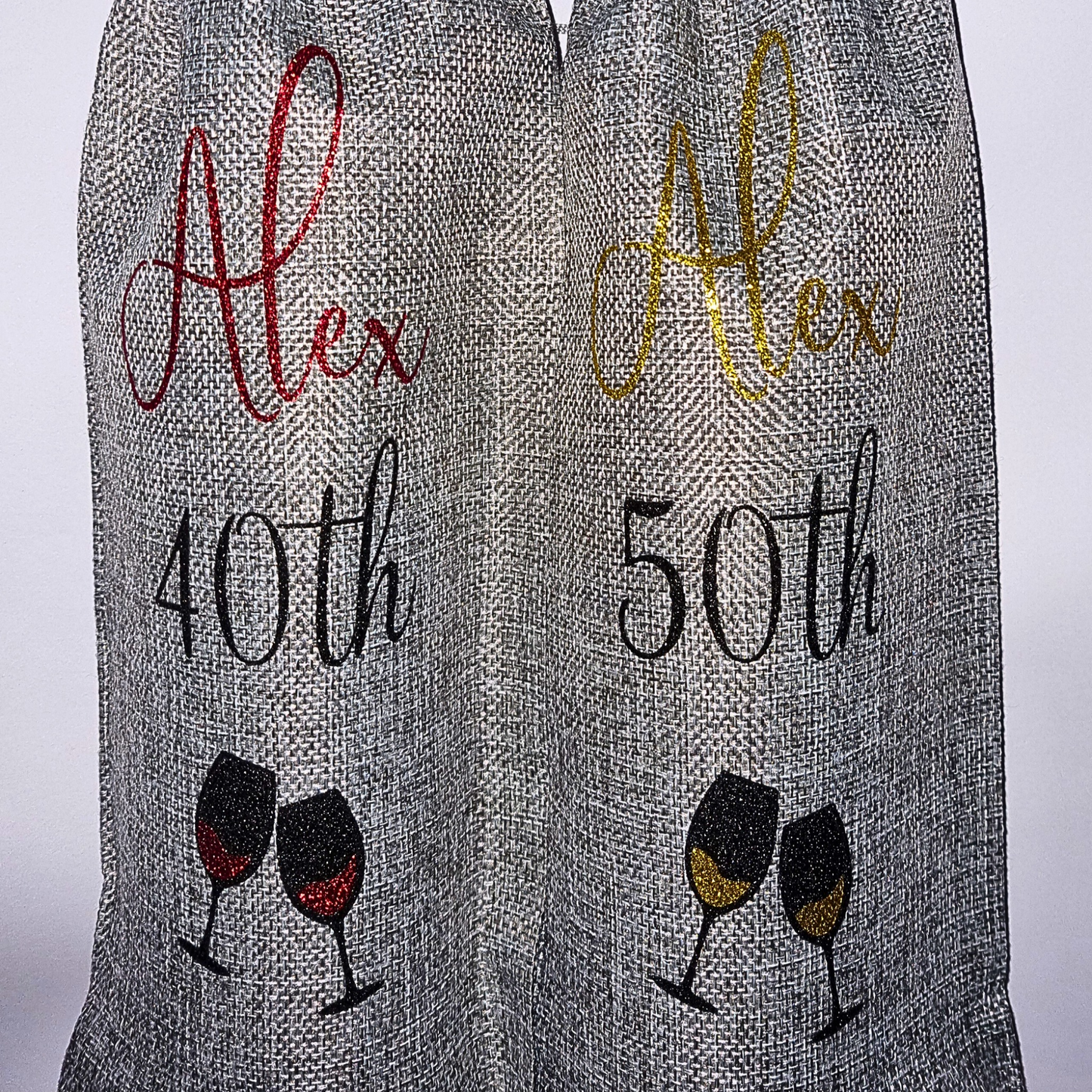 Two personalised wine bottle gift bags with the name 'Alex' and ages 40th & 50th in glitter vinyl on a plain background