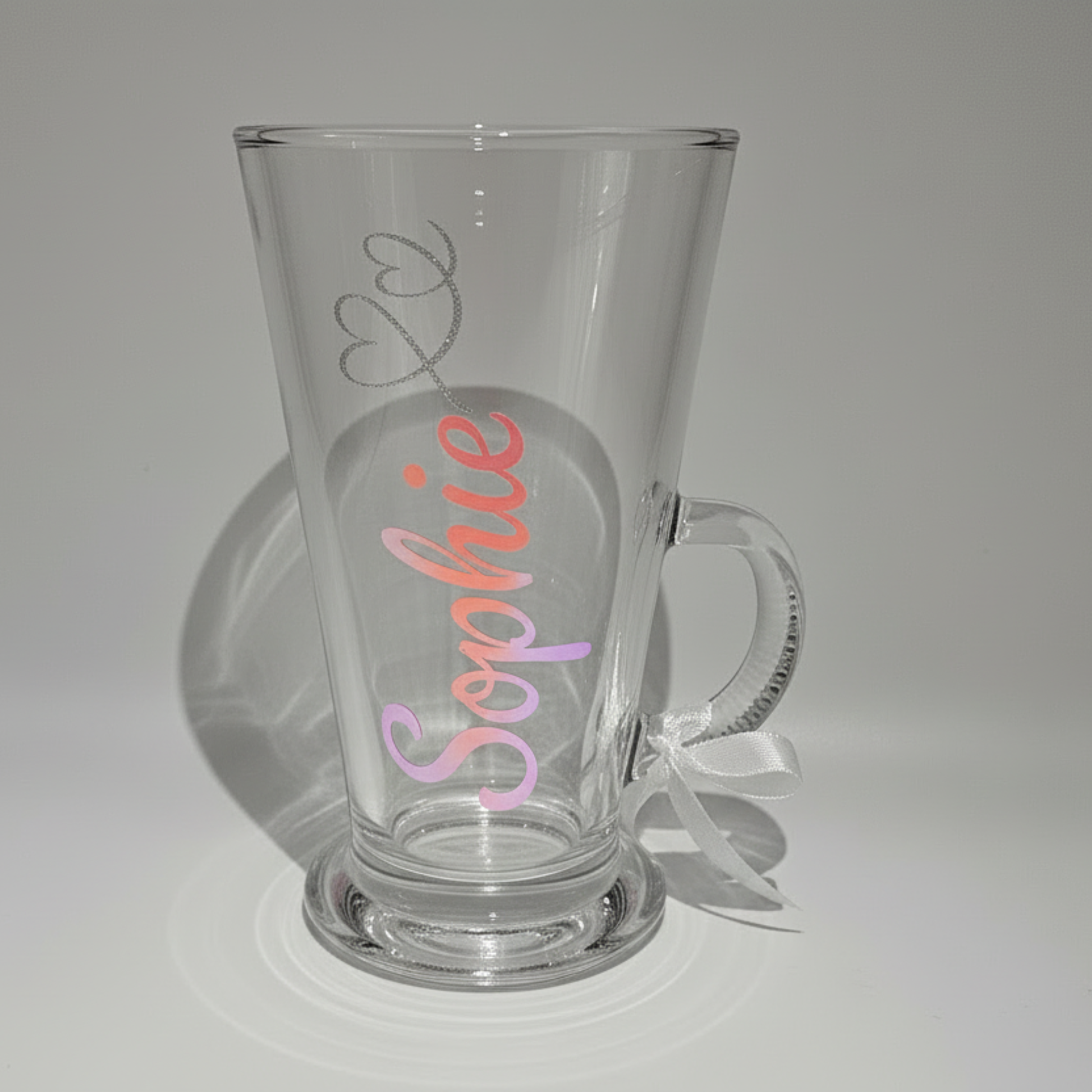 Personalised clear glass mug with the name 'Sophie' on it in a pink & coral holographic vinyl against a plain background.