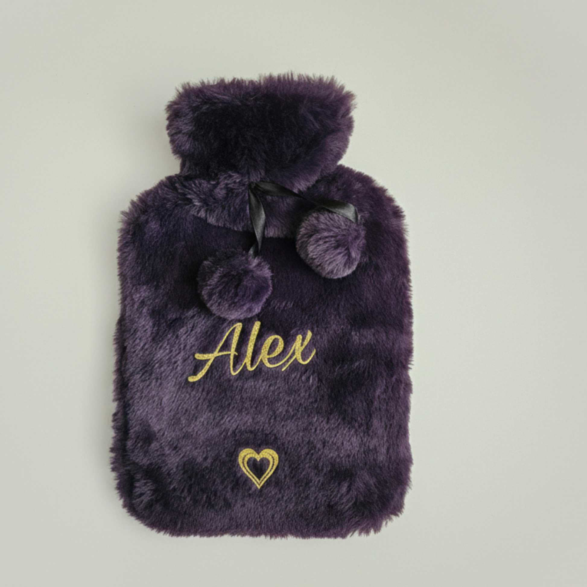 Personalised faux fur hot water bottle & pom poms in purple with the name 'Alex' in a gold glitter vinyl text on a light grey background
