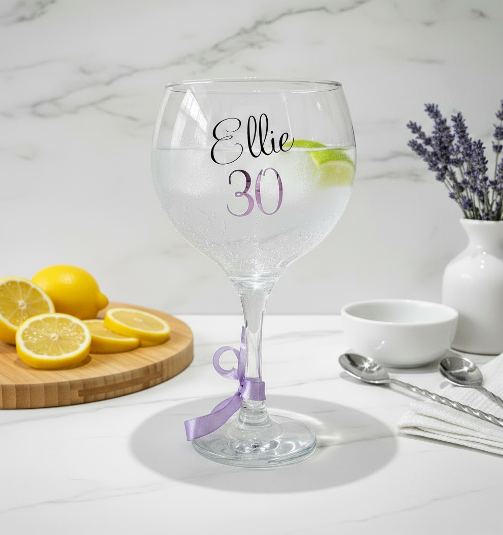 A clear glass with the name 'Ellie' on a white surface. Has a background  of lavender in a vase with a board of lemon slices