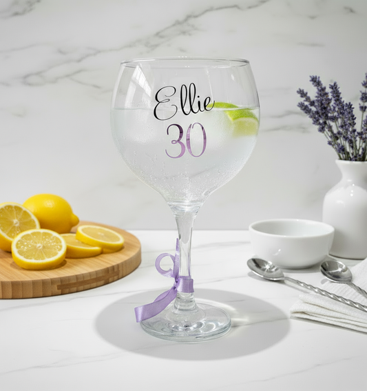 A clear glass with the name 'Ellie' on a white surface. Has a background  of lavender in a vase with a board of lemon slices