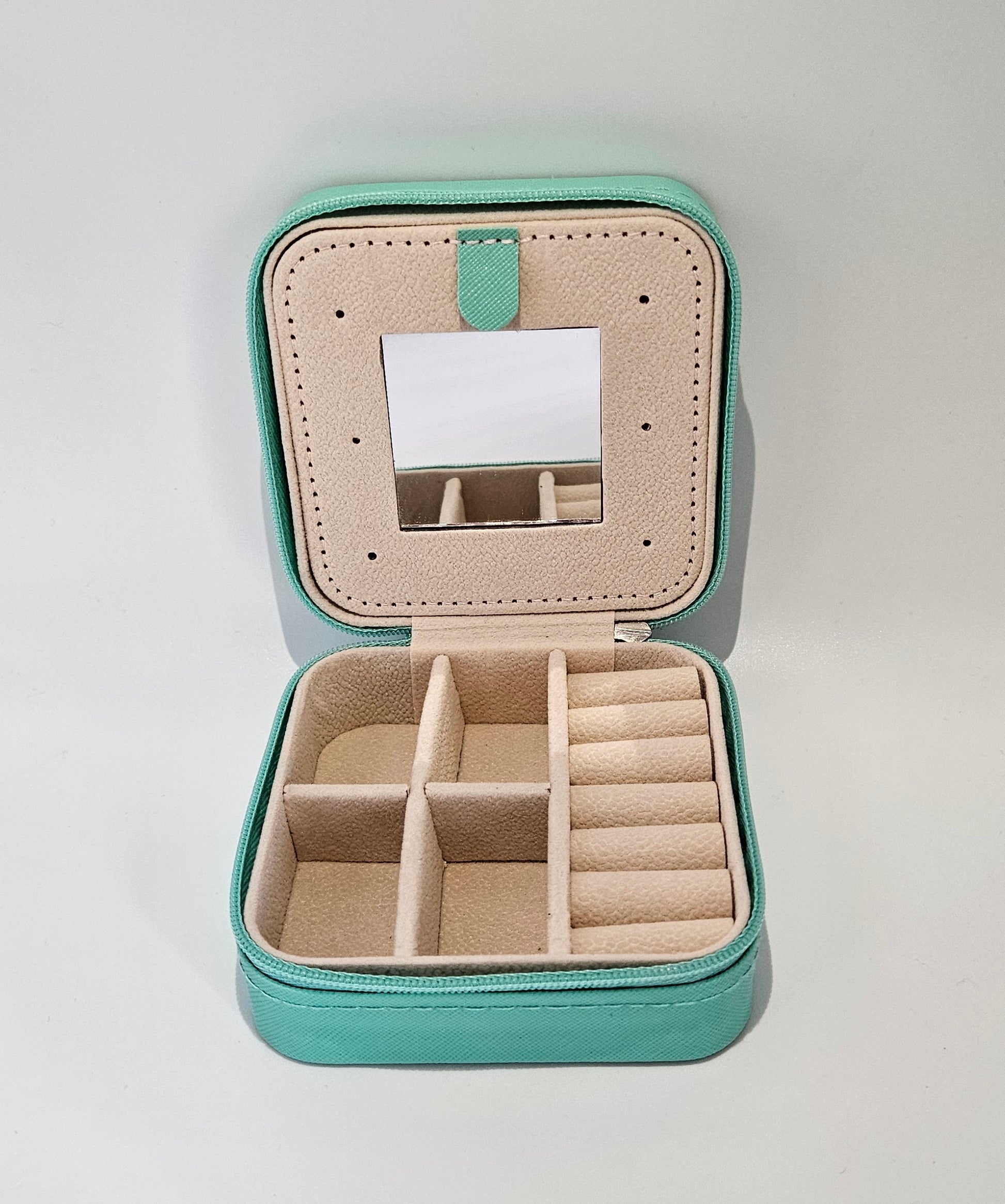Interior of a travel zip jewellery box with mirror, ring rolls & compartments for earings & necklaces on a plain background.