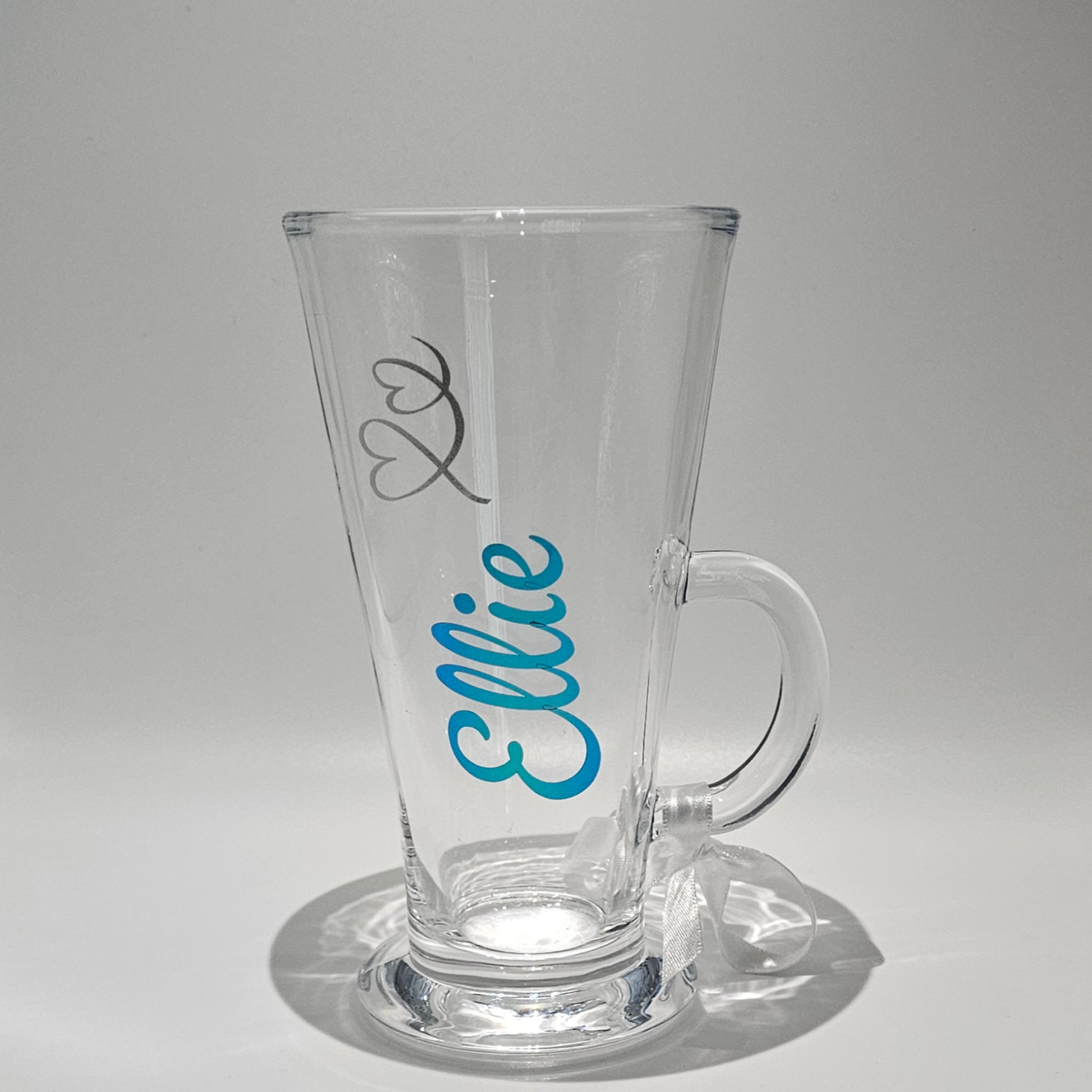 Personalised clear glass latte coffee mug with the name 'Ellie' on it in blue chrome vinyl against a plain background