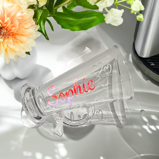 Clear latte glass with the name 'Sophie' & heart feature. Styled on a white satin drape with orange flower  & ribbon to the handle