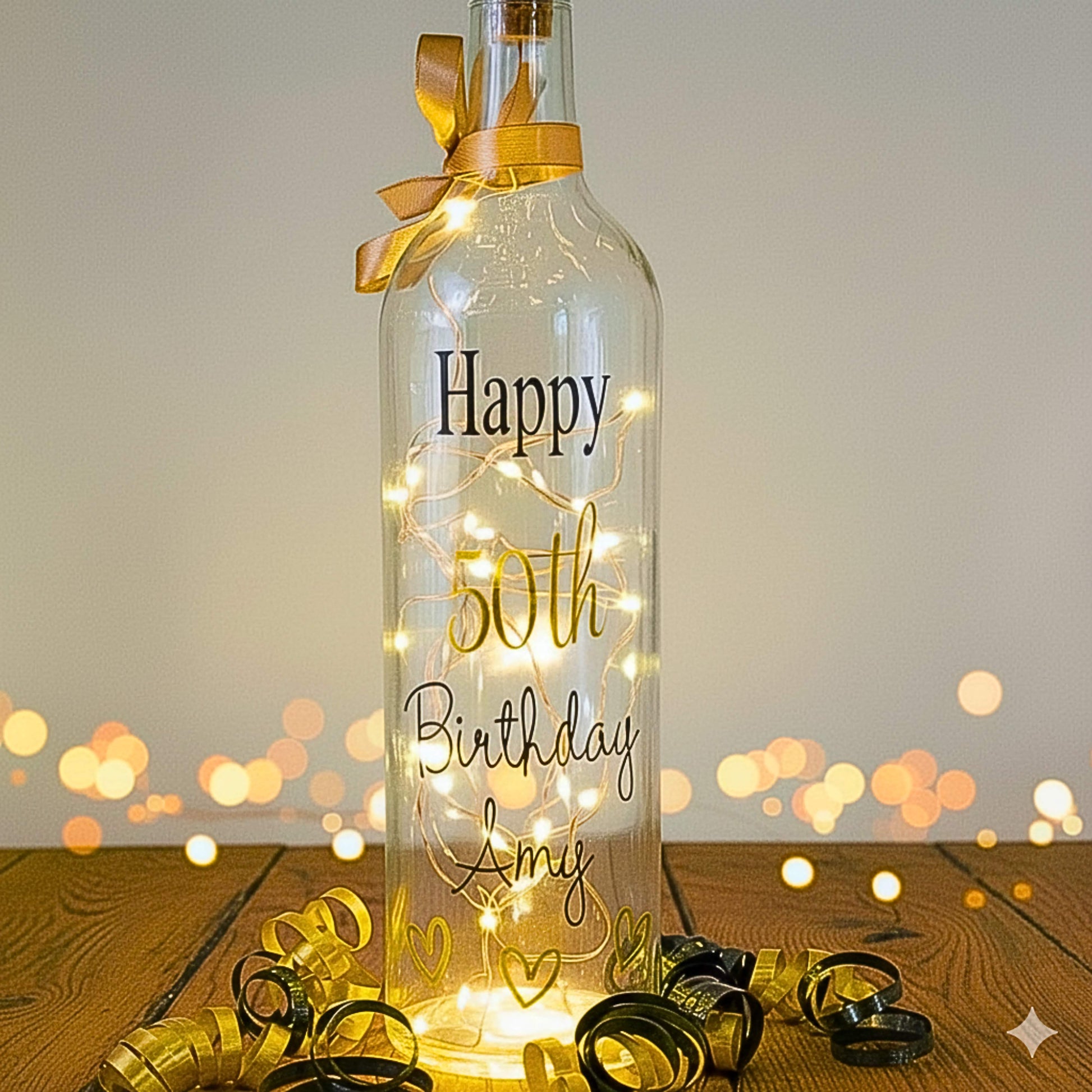 Decorative bottle with 'Happy 50th Birthday Amy' text and string lights on a wooden surface.