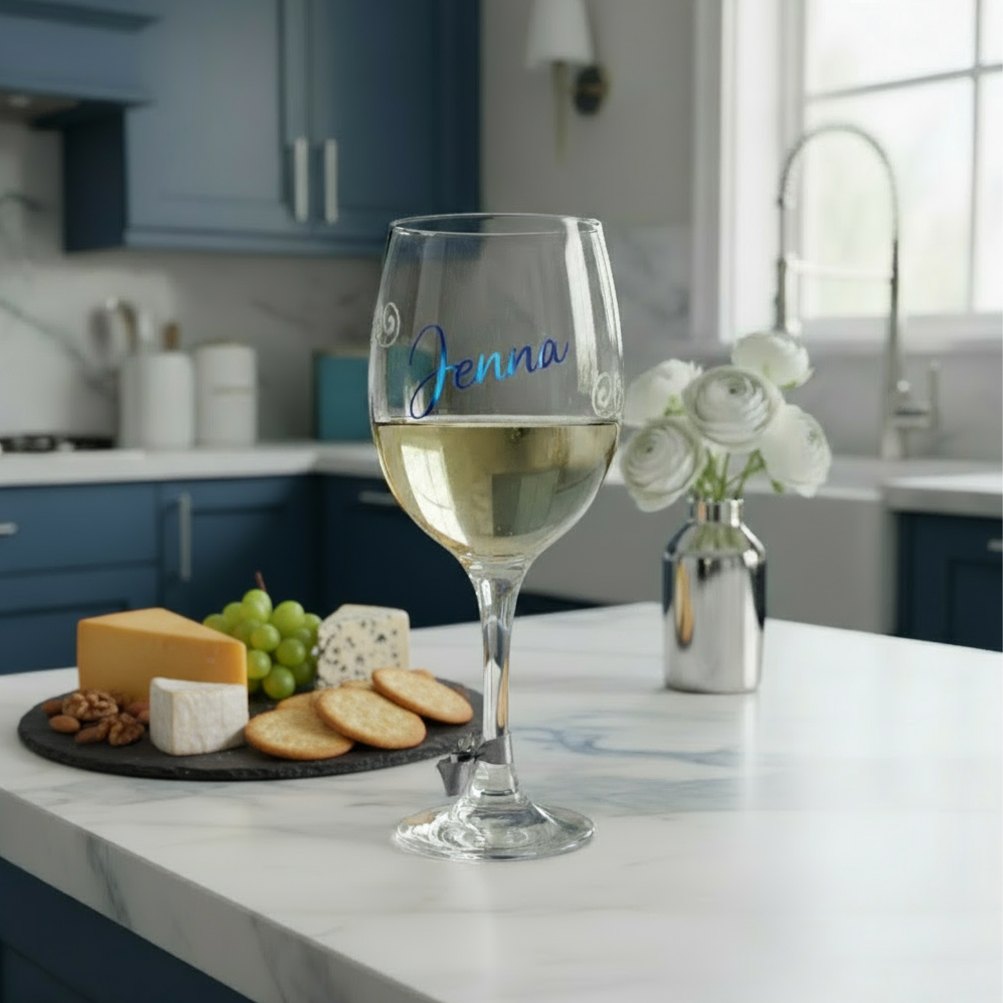 Personalised stemmed wine glass with 'Jenna' in blue holographic vinyl on a kitchen counter with a cheese and fruit platter.