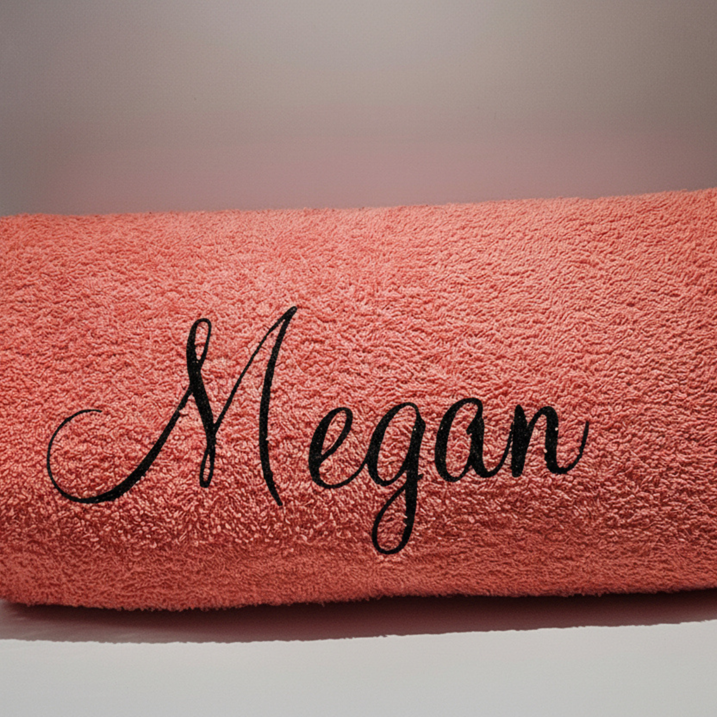 Personalised pink beach towel with the name 'Megan' on it in a black glitter vinyl text on a plain background.