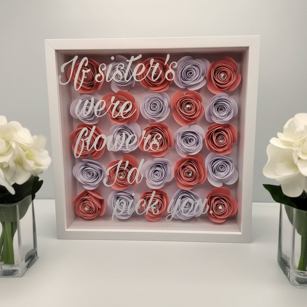 Personalised 3D shadow box with a display of pink & white flowers in a white frame & text in white vinyl on a glass front. Sat on a shelf with small vases of white flowers each side.