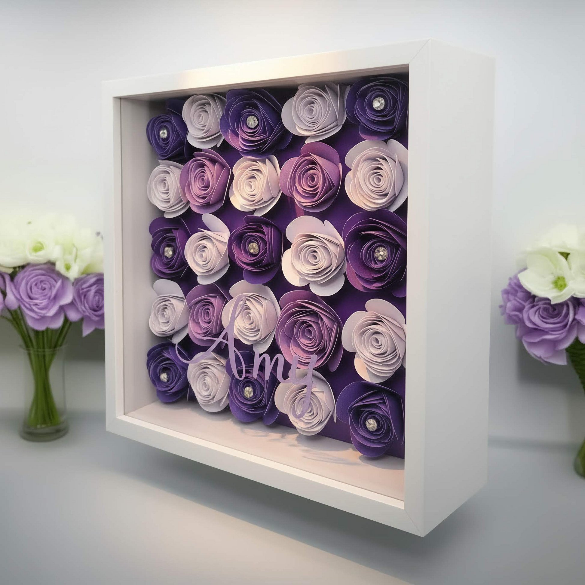 Personalised shadow box with the name 'Amy' on it with a purple, lilac & white floral display sat next to a vase of flowers