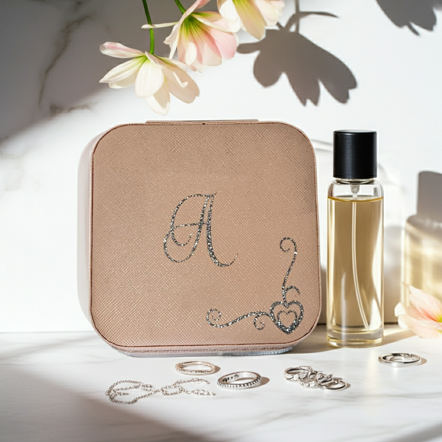 Personalised pink square jewellery box with the initial 'A' on it with a heart swirl border in silver glitter vinyl. Placed on a white marble surface next to small jewellery pieces and a purfume bottle.