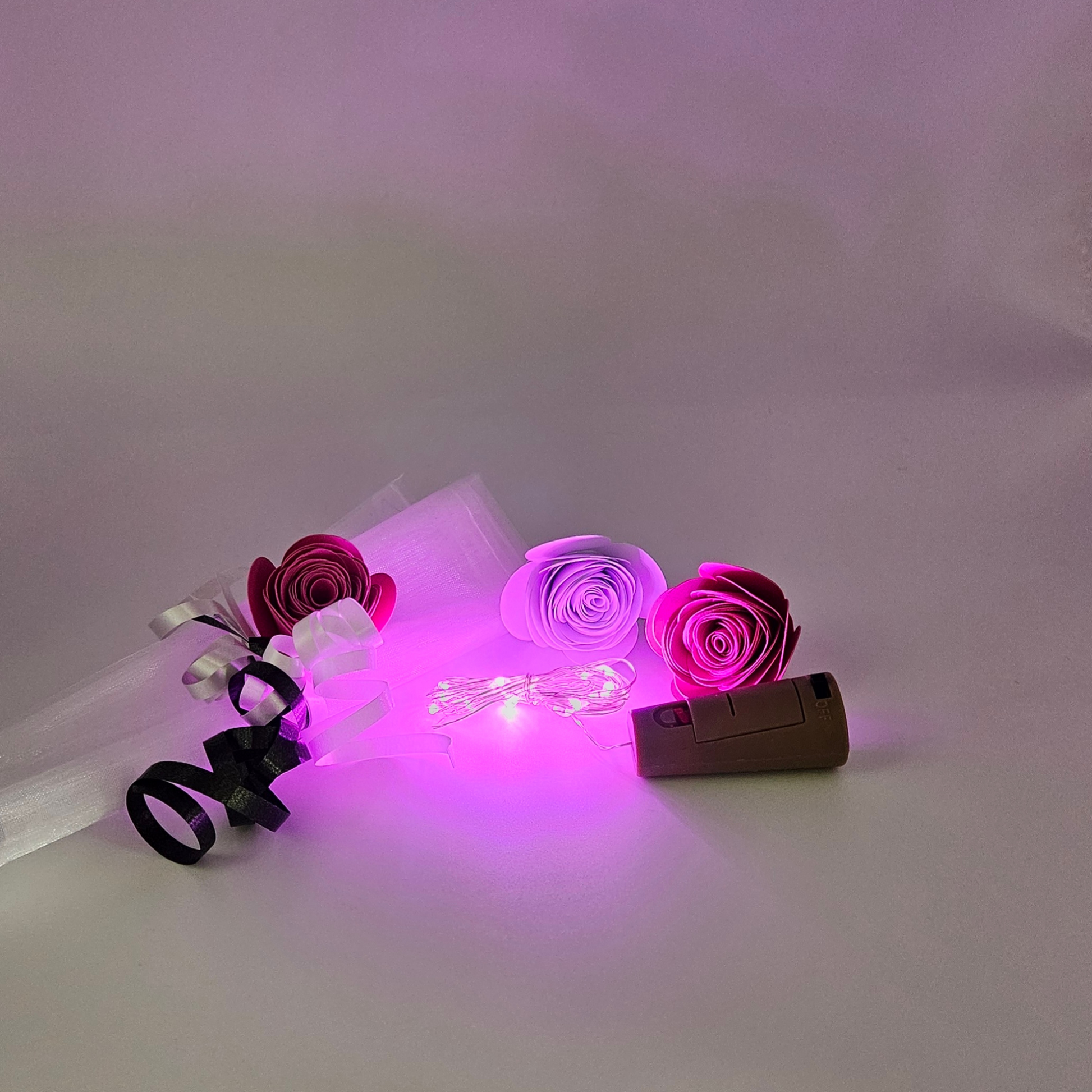 Pink LED bottle lights next to an organza gift bag & satin curling ribbons on a white background