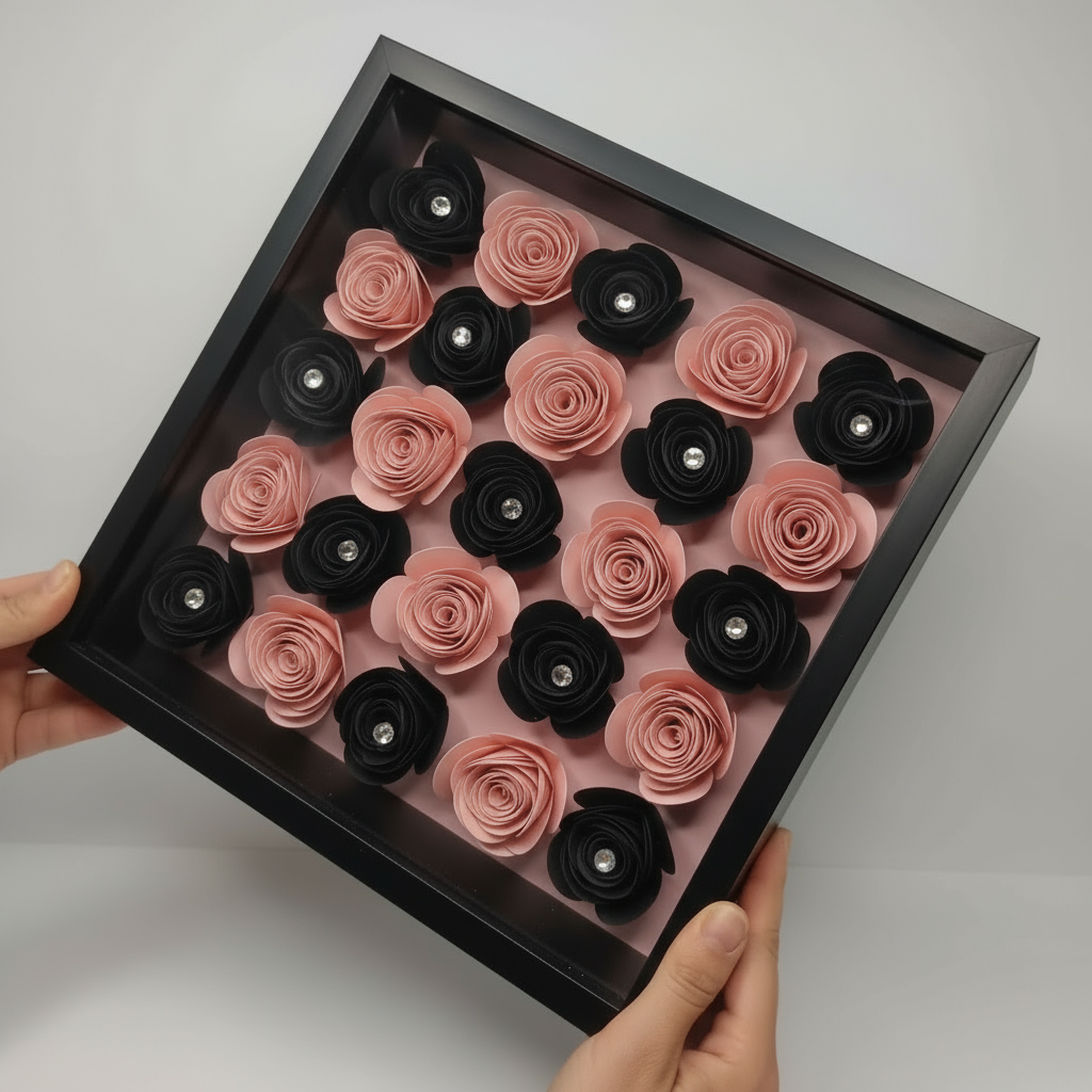 3D Shadow box with pink & black flower arrangements in a black frame held up on a white background
