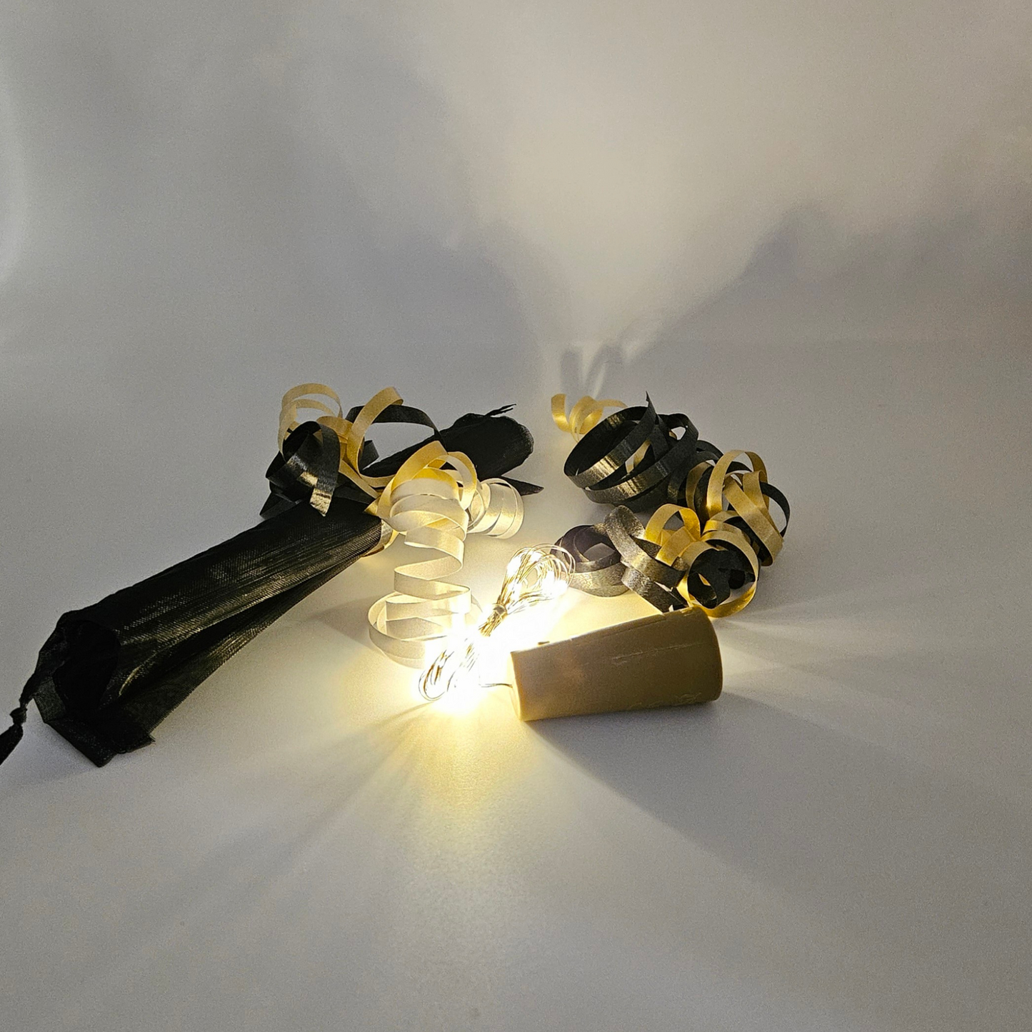 Warm white LED bottle lights next to an organza gift bag with satin curling ribbons around on a white background