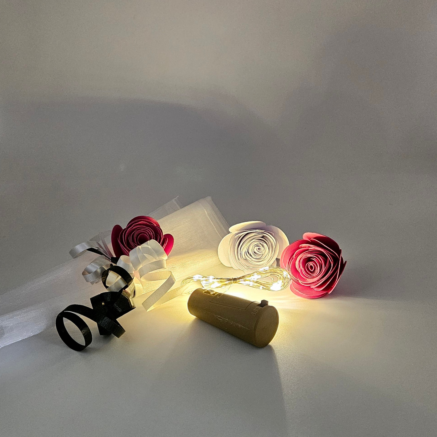 LED warm white bottle lights next to an organza gift bag & satin curlings ribbons on a plain background