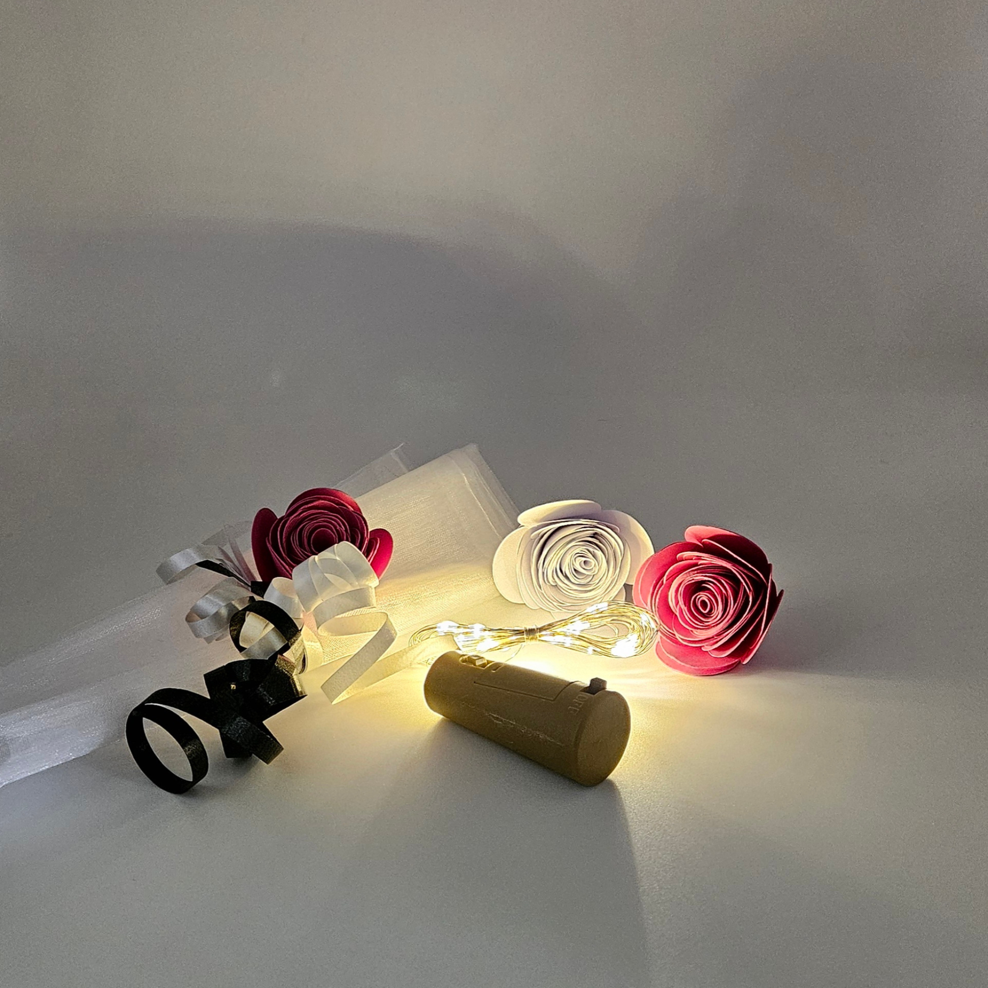 LED warm white bottle lights next to an organza gift bag & satin curlings ribbons on a plain background