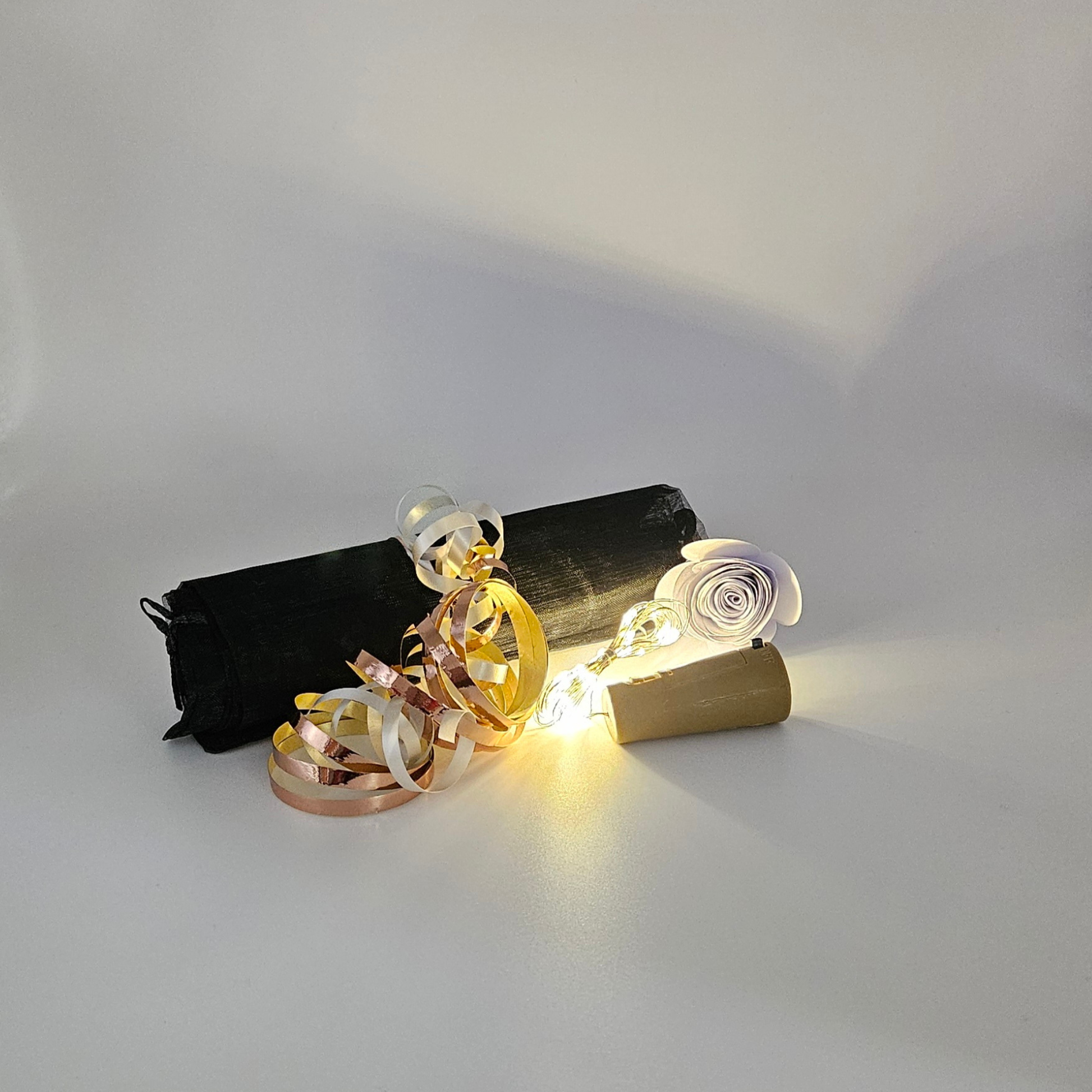 Warm white LED bottle lights next to an organza gift bag tied with satin rose gold & silver curling ribbons on a plain background